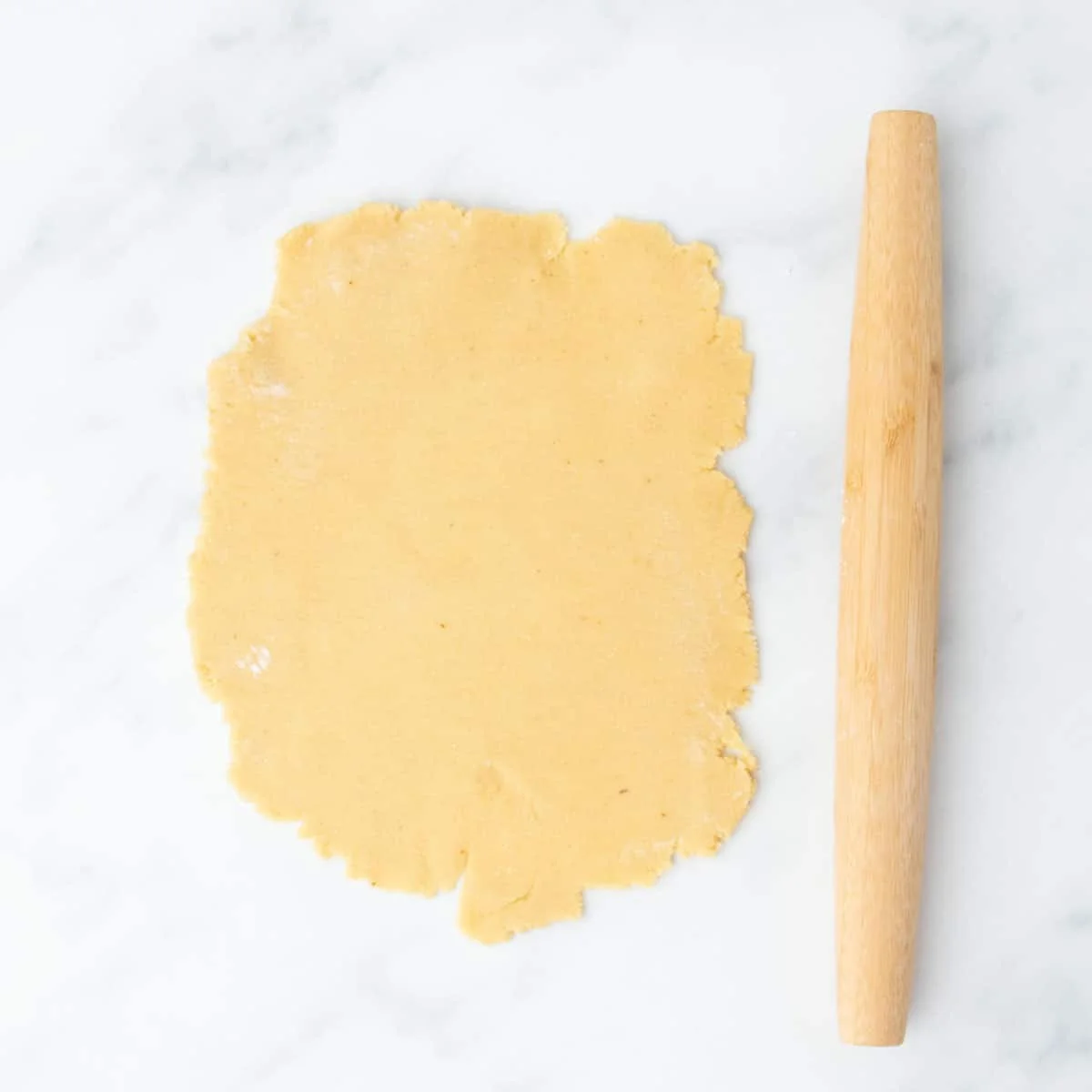 Dough rolled into a rough rectangle next to a wooden rolling pin.
