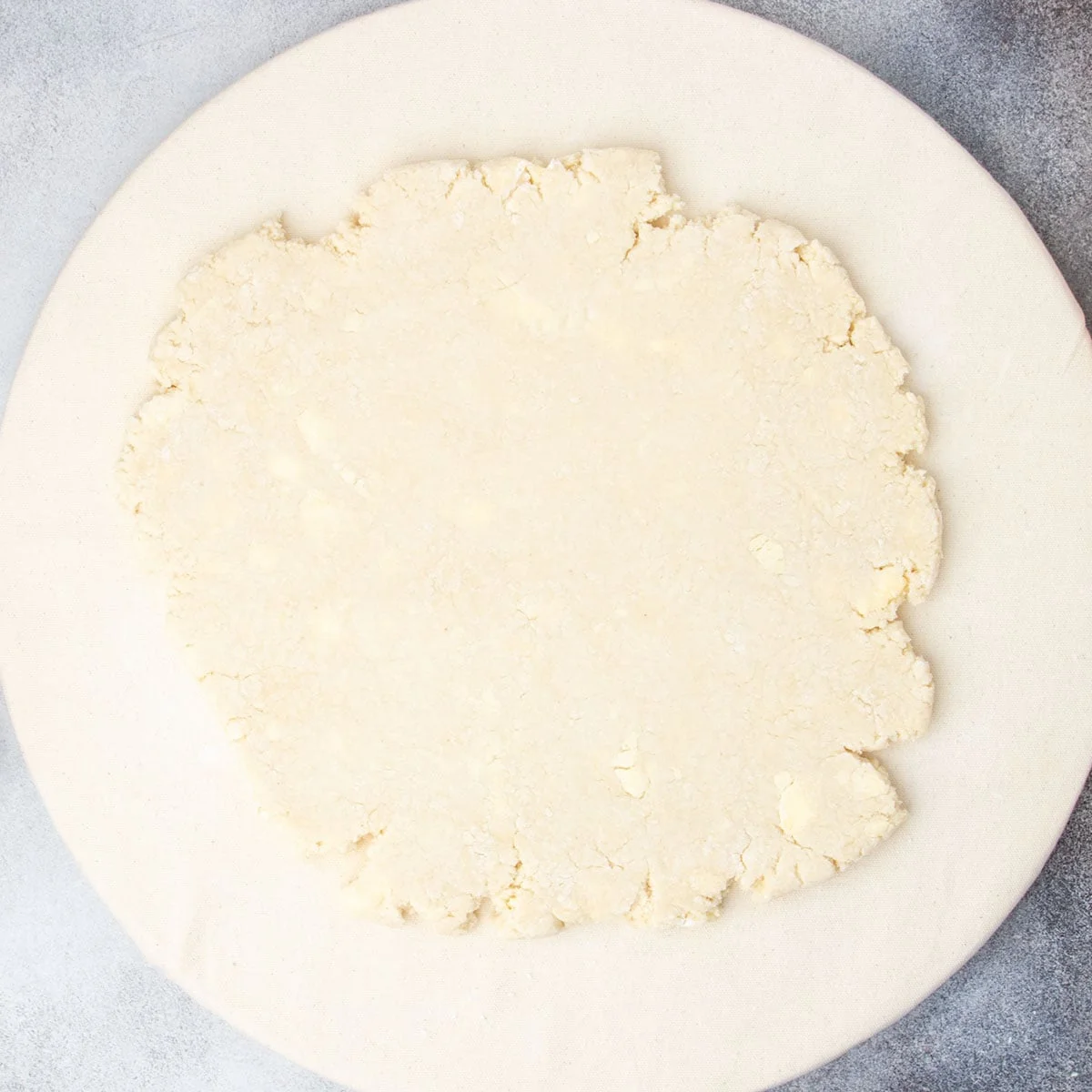 Dough rolled out into a rough round on a tan round cloth.