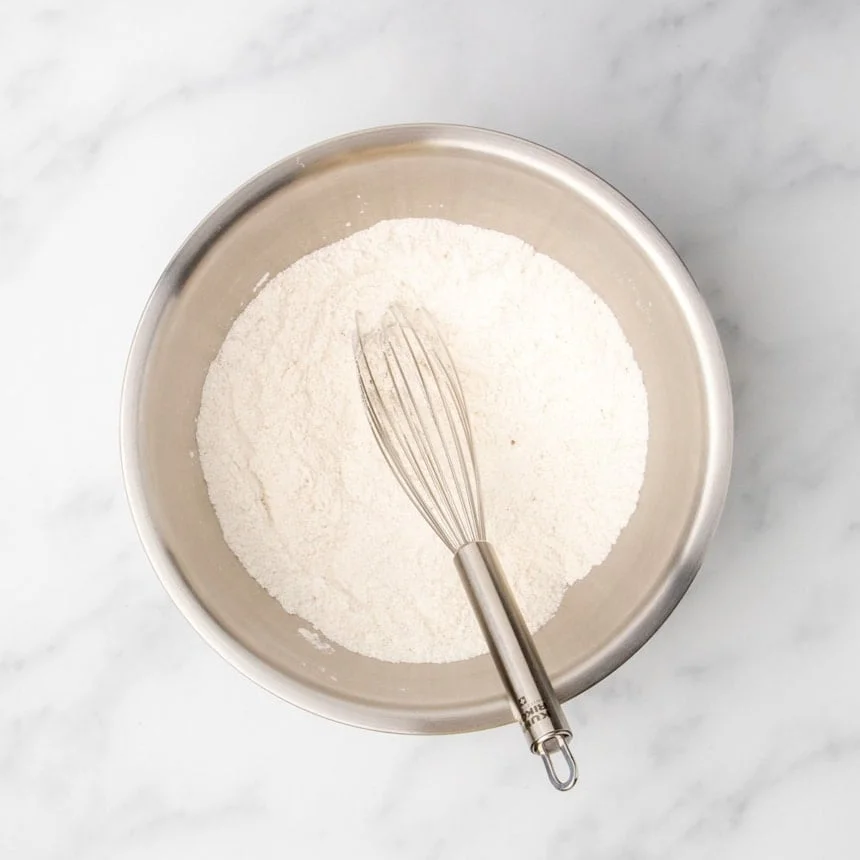 Dry ingredients whisked together in a stainless steel mixing bowl with a whisk.