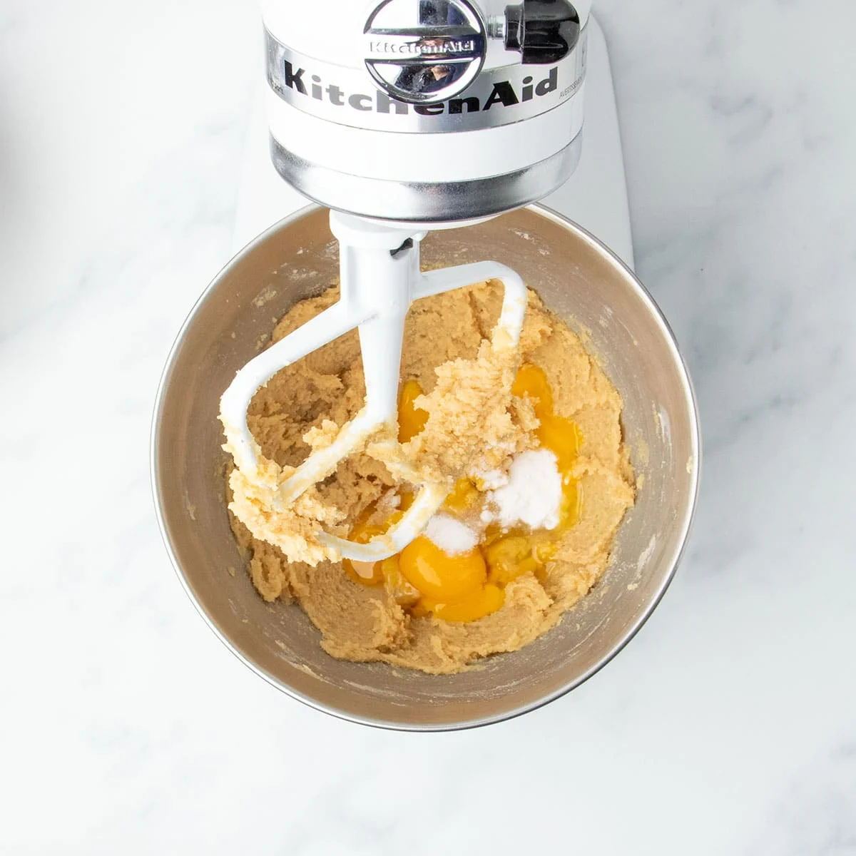 Egg, egg yolks, and leavening added to creamed butter-sugar mixture in a stand mixer.