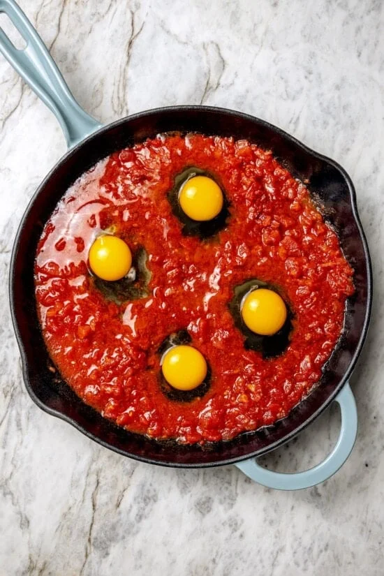 Eggs cracked into tomato sauce in skillet
