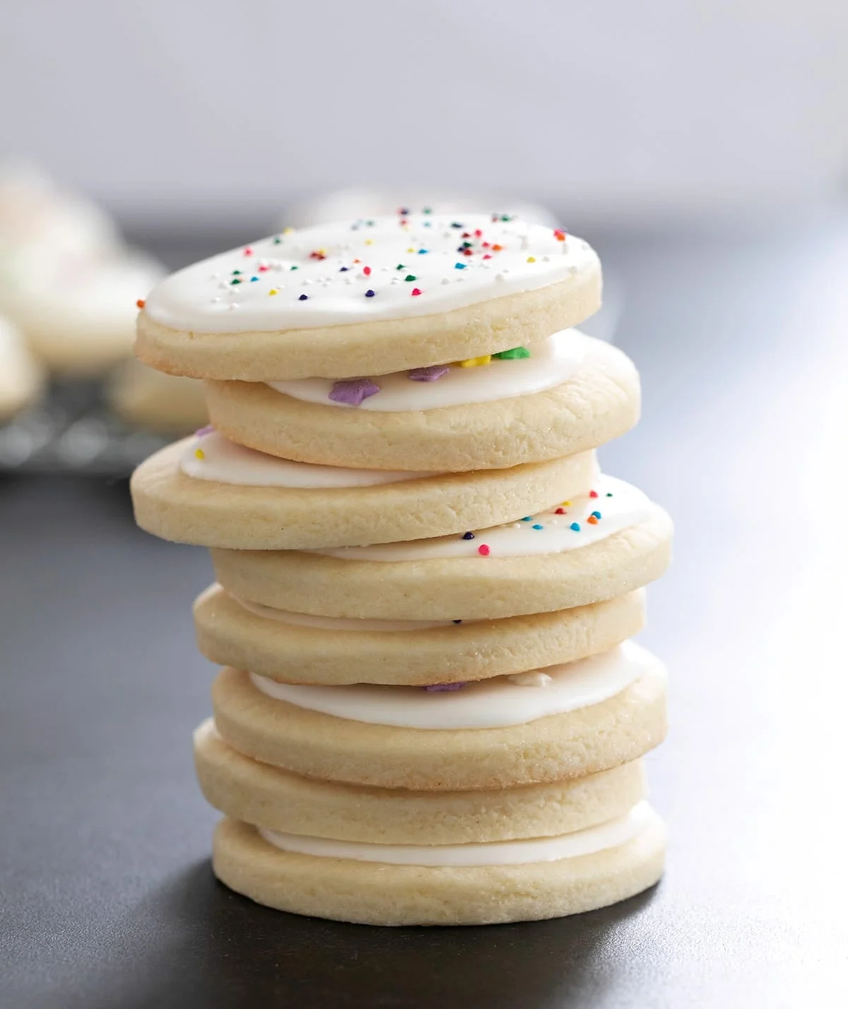 Eight round sugar cookies with white frosting in a vertical stack.