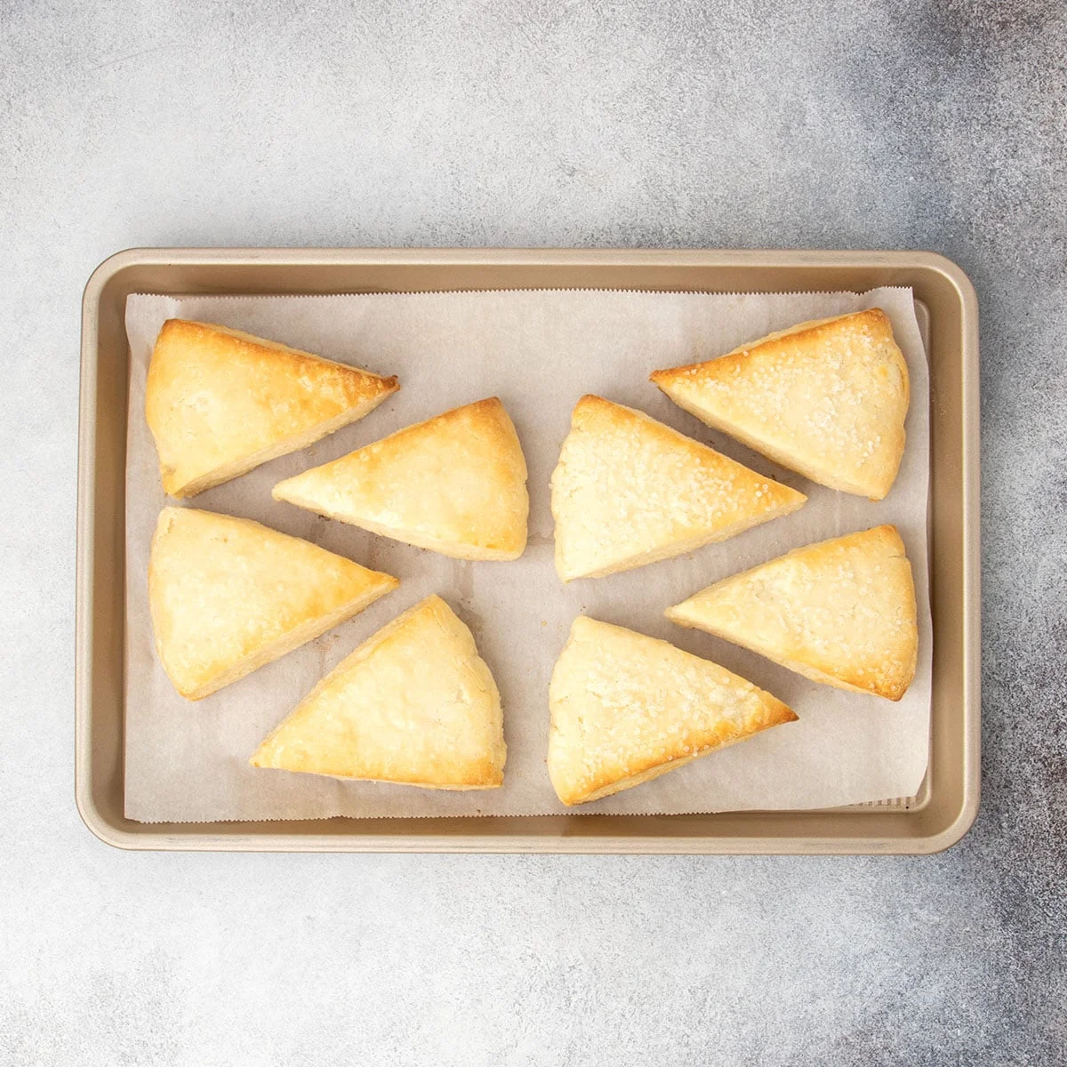 Eight scones on parchment lined tray just baked from the oven with light brown tops and browned edges.