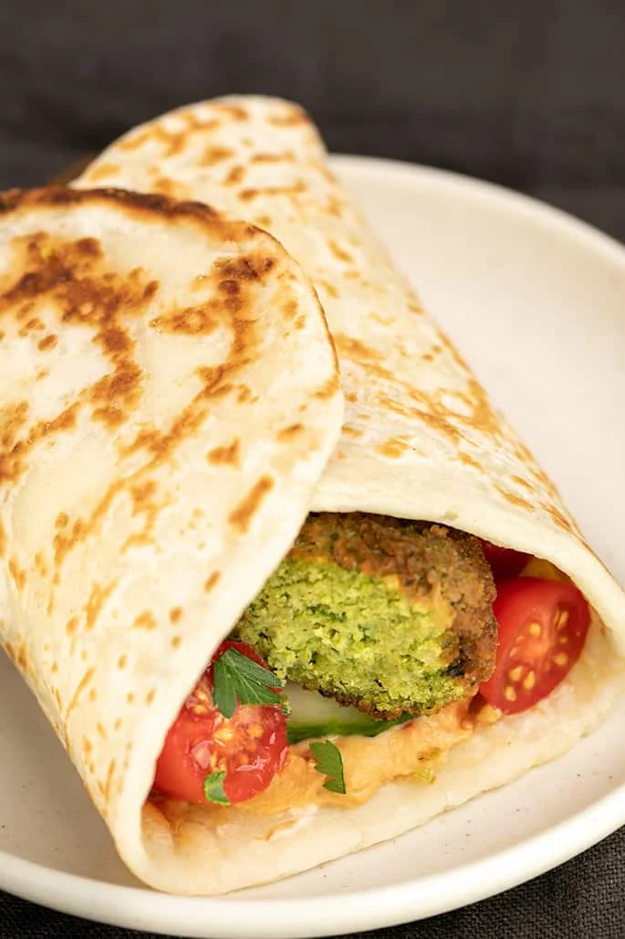 Falafel sliced in half with tomatoes and hummus in flatbread on small white plate