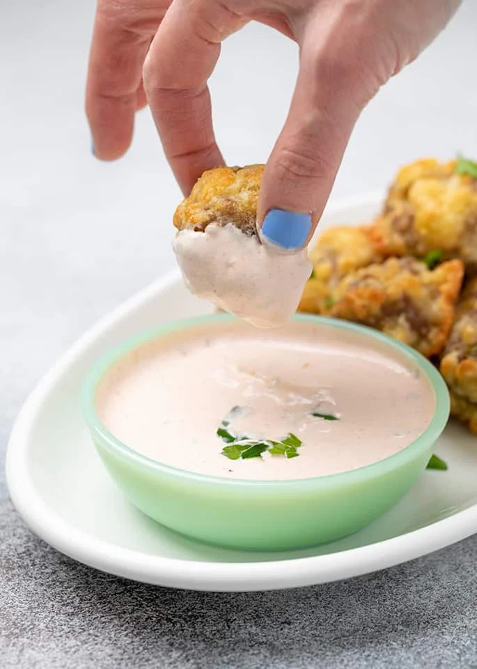Fingers holding sausage ball dipped in light orange sauce