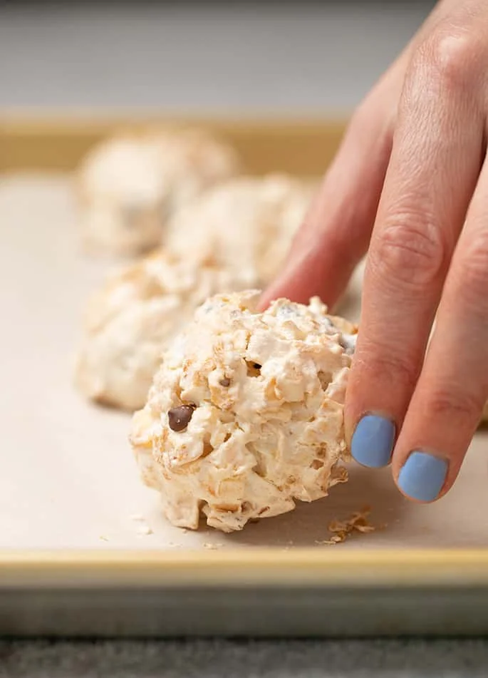 Fingers picking up baked macaroon from baking tray