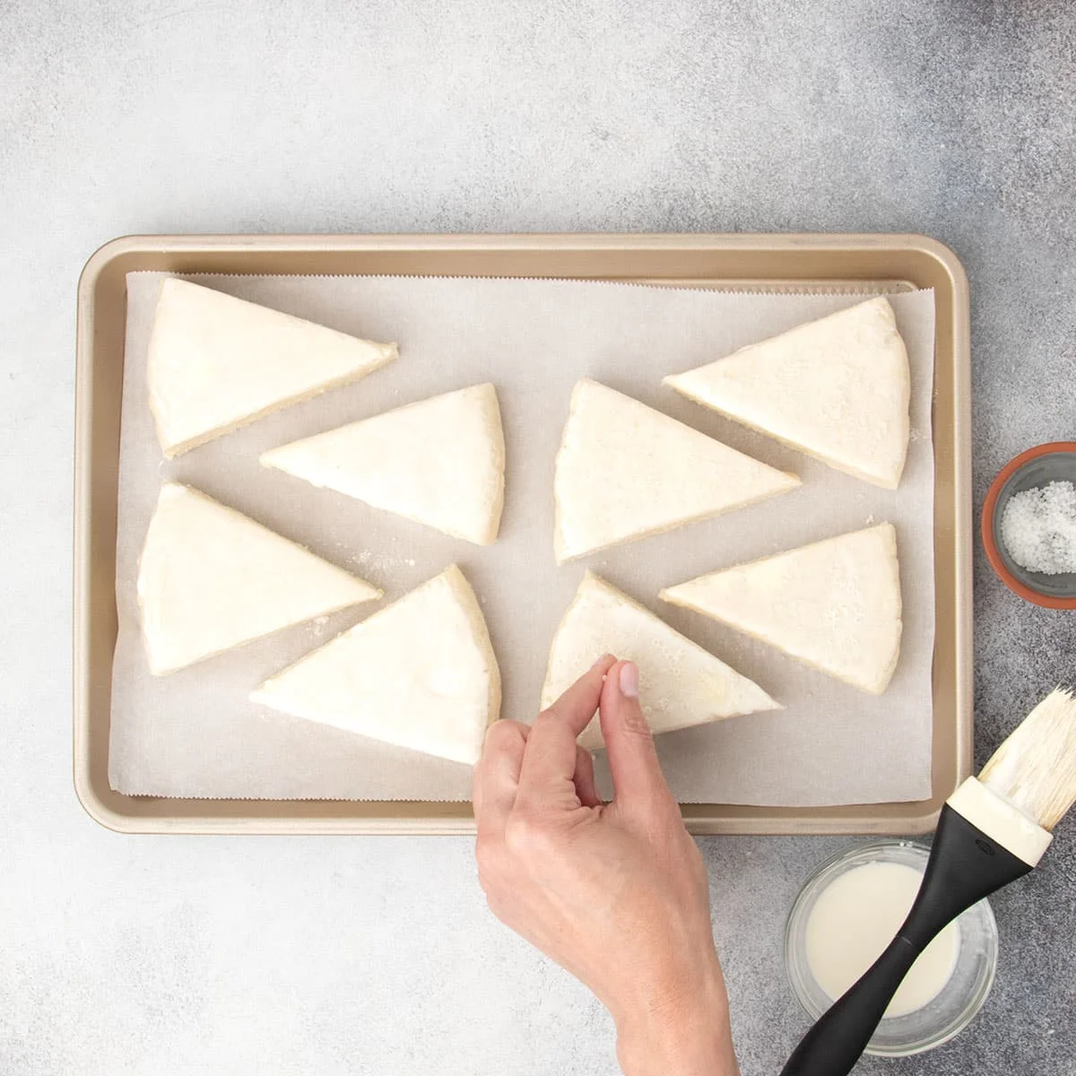 Fingers sprinkling coarse sugar on top of raw scone triangle.
