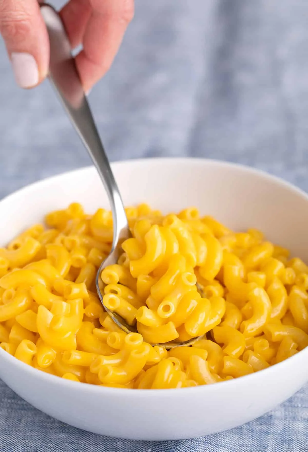 Fingers taking a spoonful of elbow mac and cheese in white bowl.