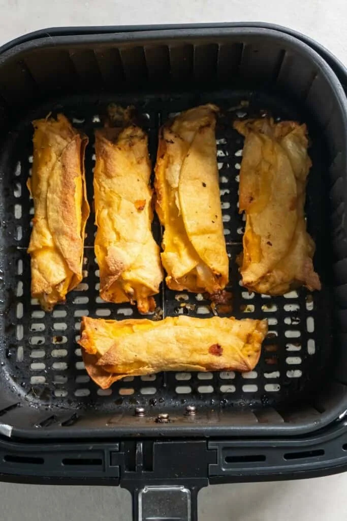 Five cooked taquitos resting in a black air fryer basket.