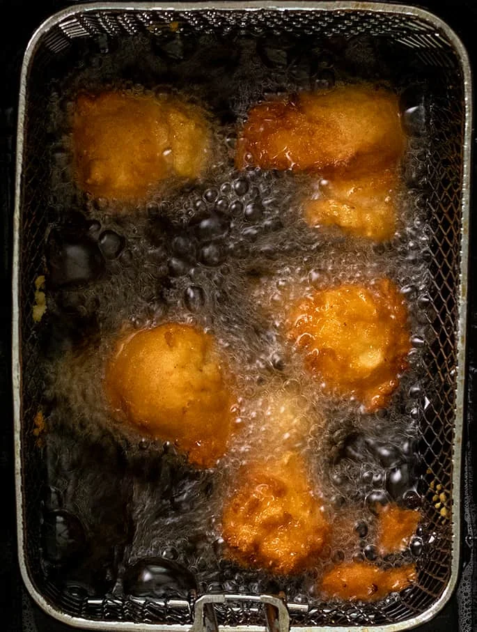 Five fritters frying in oil in frying basket overhead image