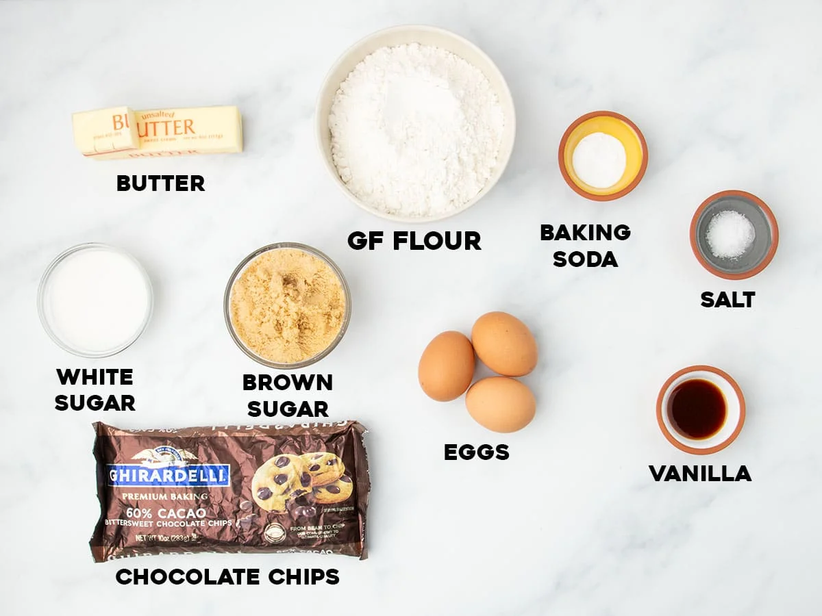 Flat lay of labeled ingredients for gluten free cookie cake, including gluten free flour, butter, sugars, chocolate chips, and vanilla.