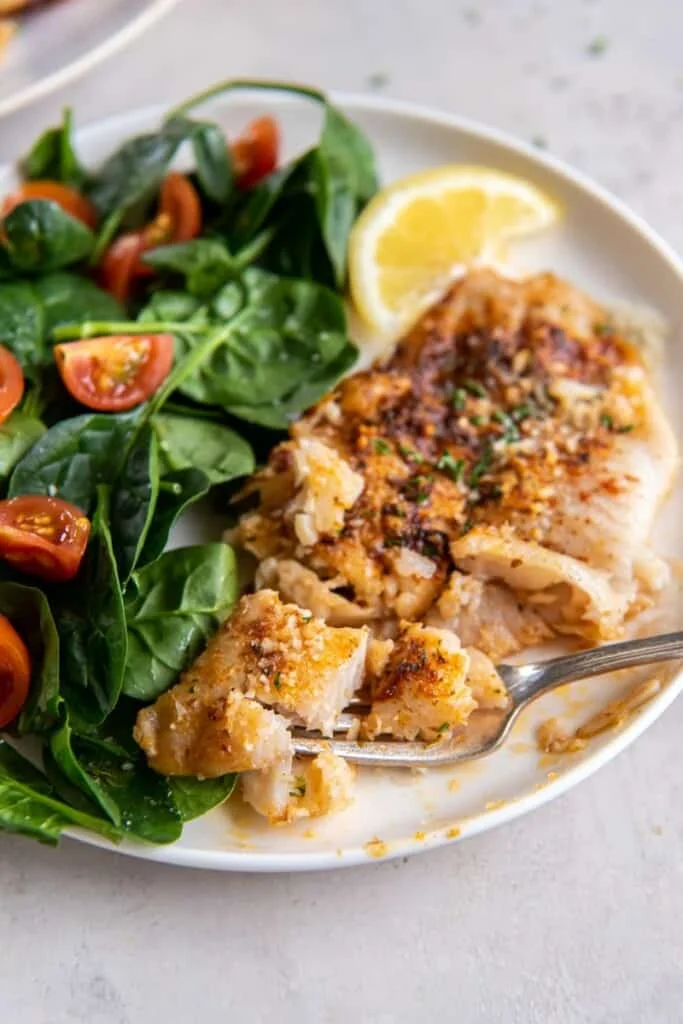 Flounder on a white plate with a salad and lemon wedge.