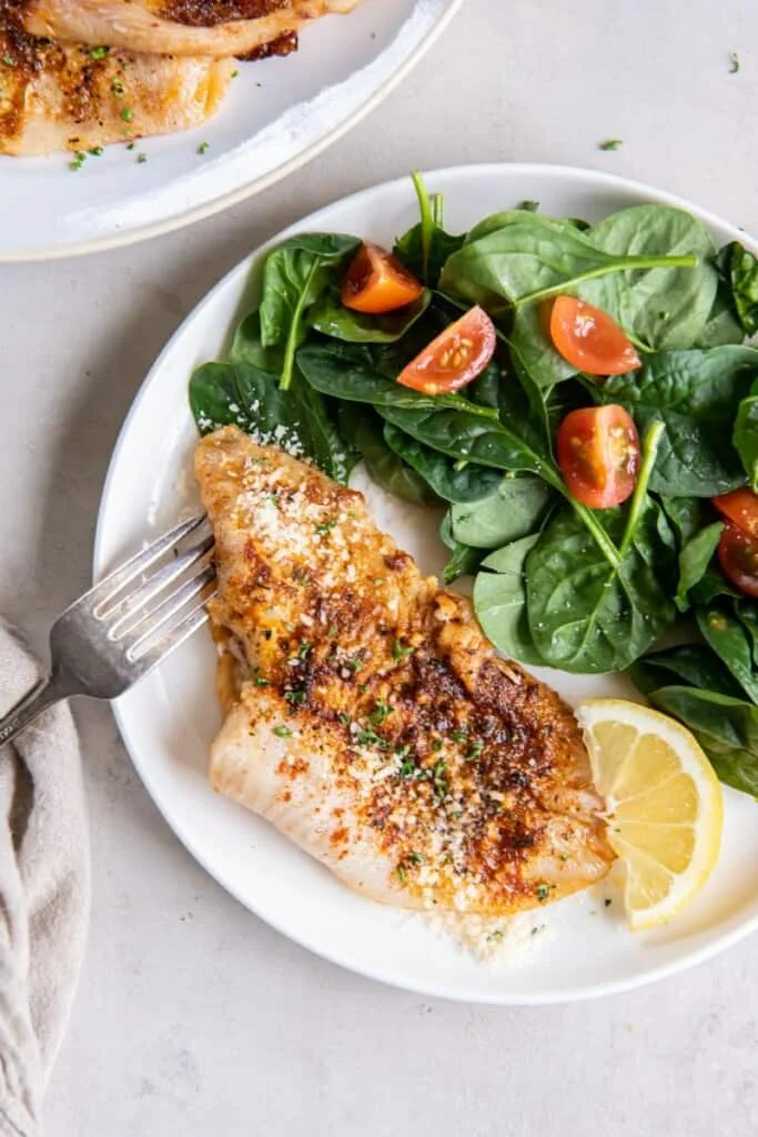 Flounder with a side salad on a white plate.