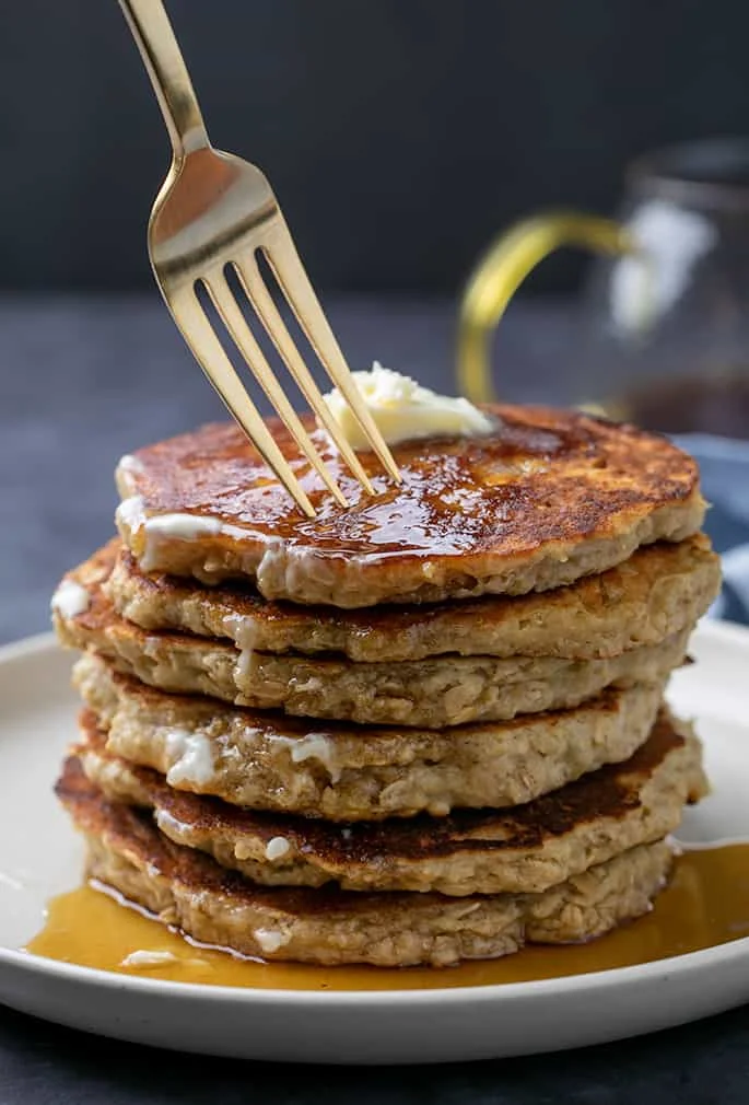 Fork above stack of oatmeal pancakes with syrup