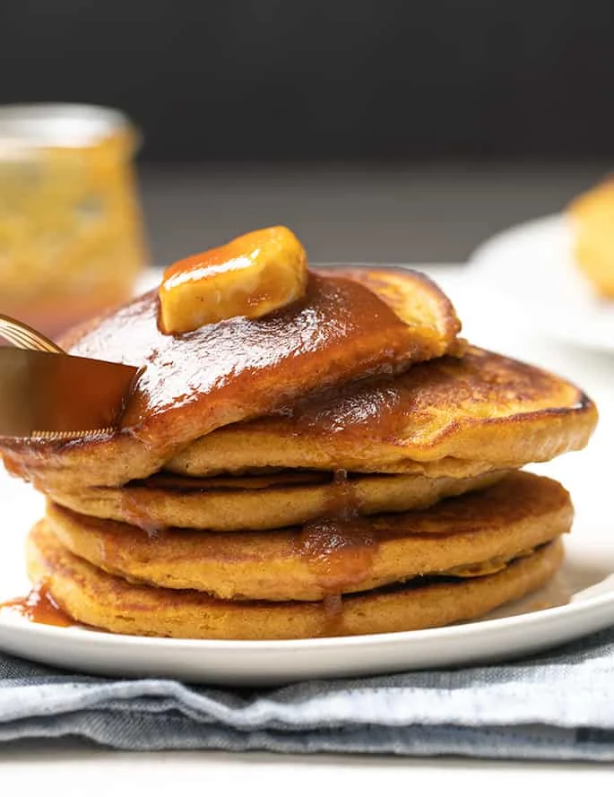 Fork and knife about to cut into stack of 5 pumpkin pancakes on white plate