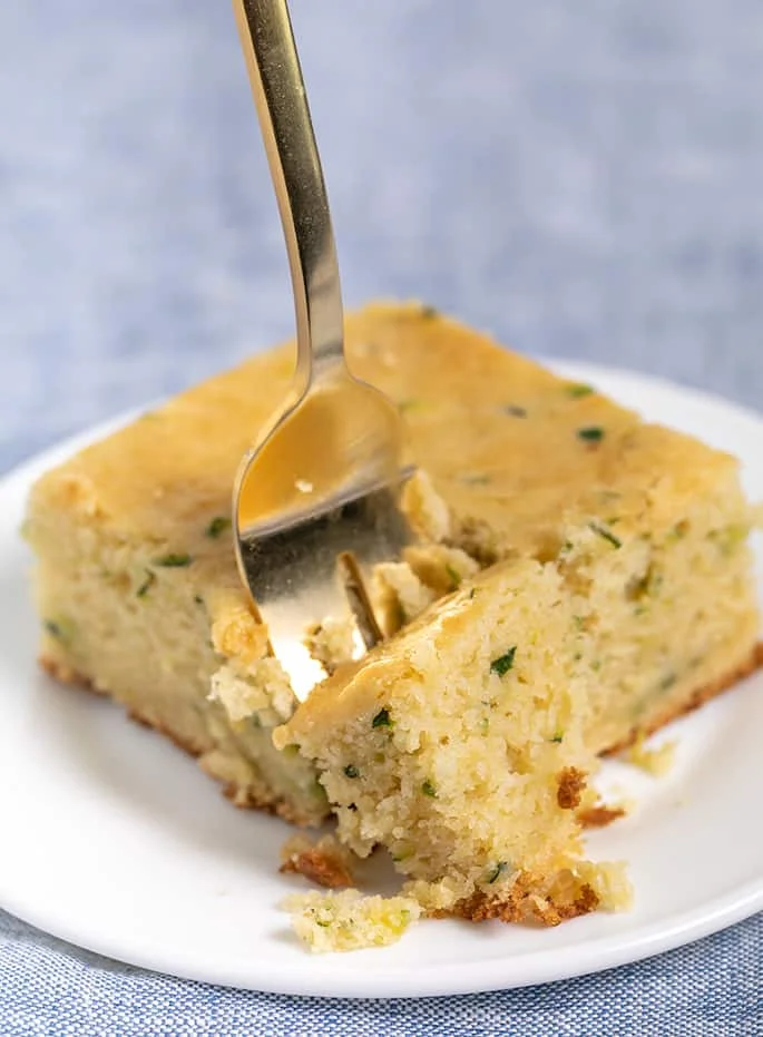 Fork taking a bite of plain zucchini cake square on small white round plate
