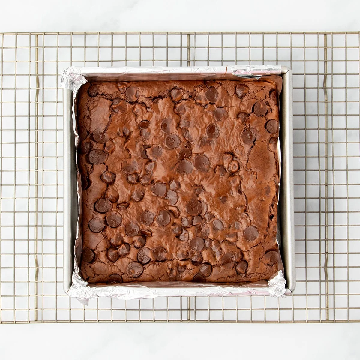 Freshly baked flourless brownies with a crinkly top, cooling in the pan on a wire rack
