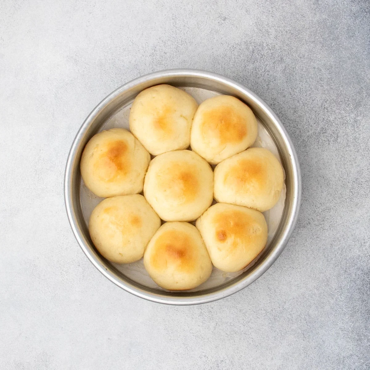 Freshly baked gluten free dinner rolls in a round pan with golden brown tops.