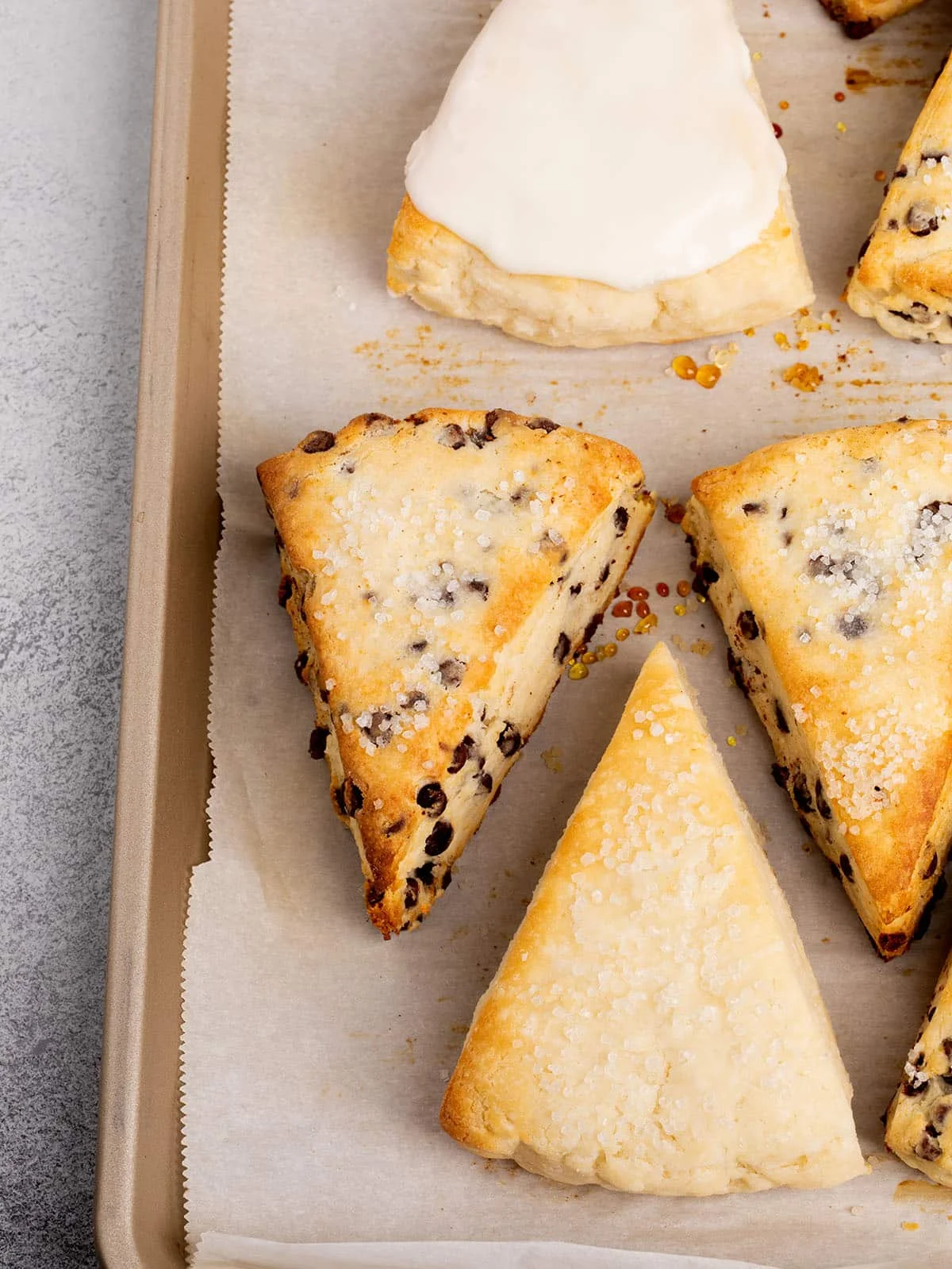 Freshly baked gluten free scones, including chocolate chip and glazed, on a parchment-lined tray.