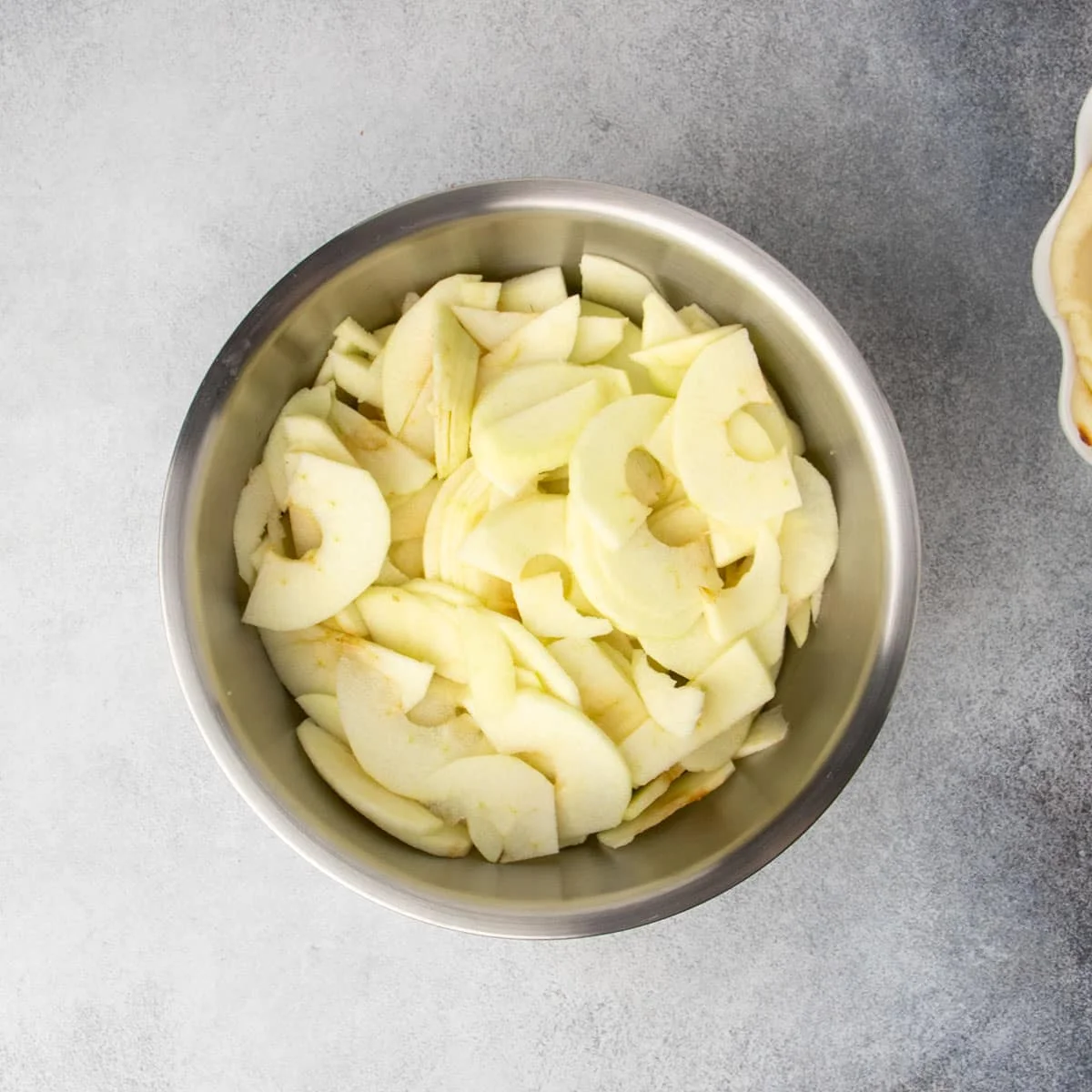 Freshly peeled and cored, thinly sliced green apples in a large metal mixing bowl.