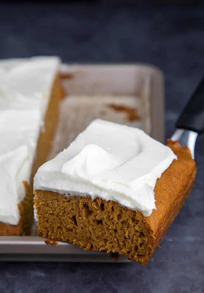 Frosted pumpkin square on spatula on edge of baking pan