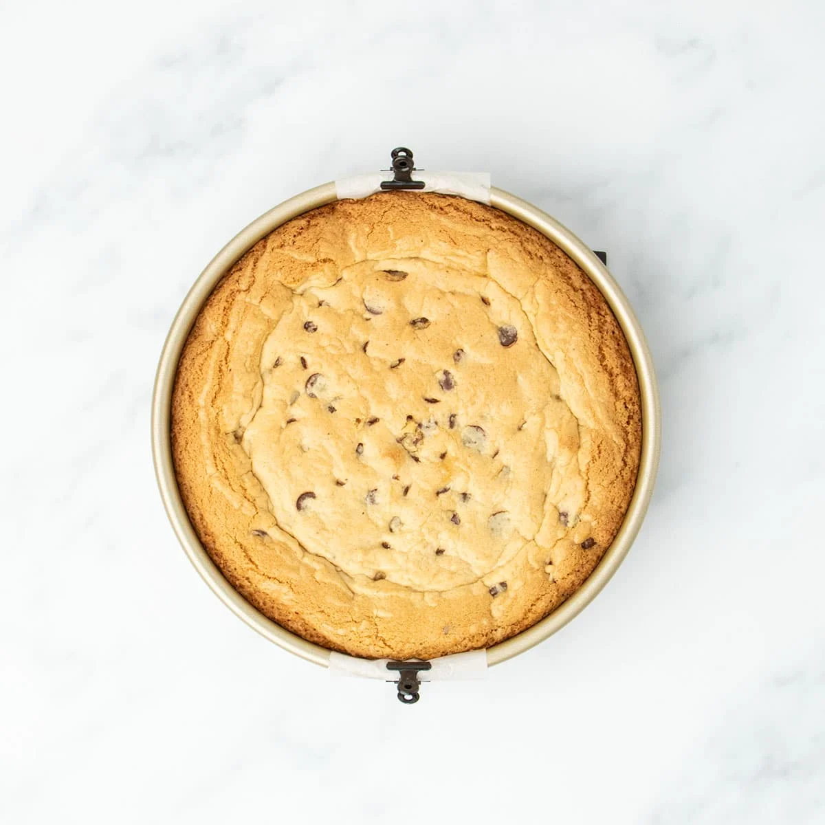 Fully baked gluten free cookie cake in the pan, golden brown and puffed with a crackled top