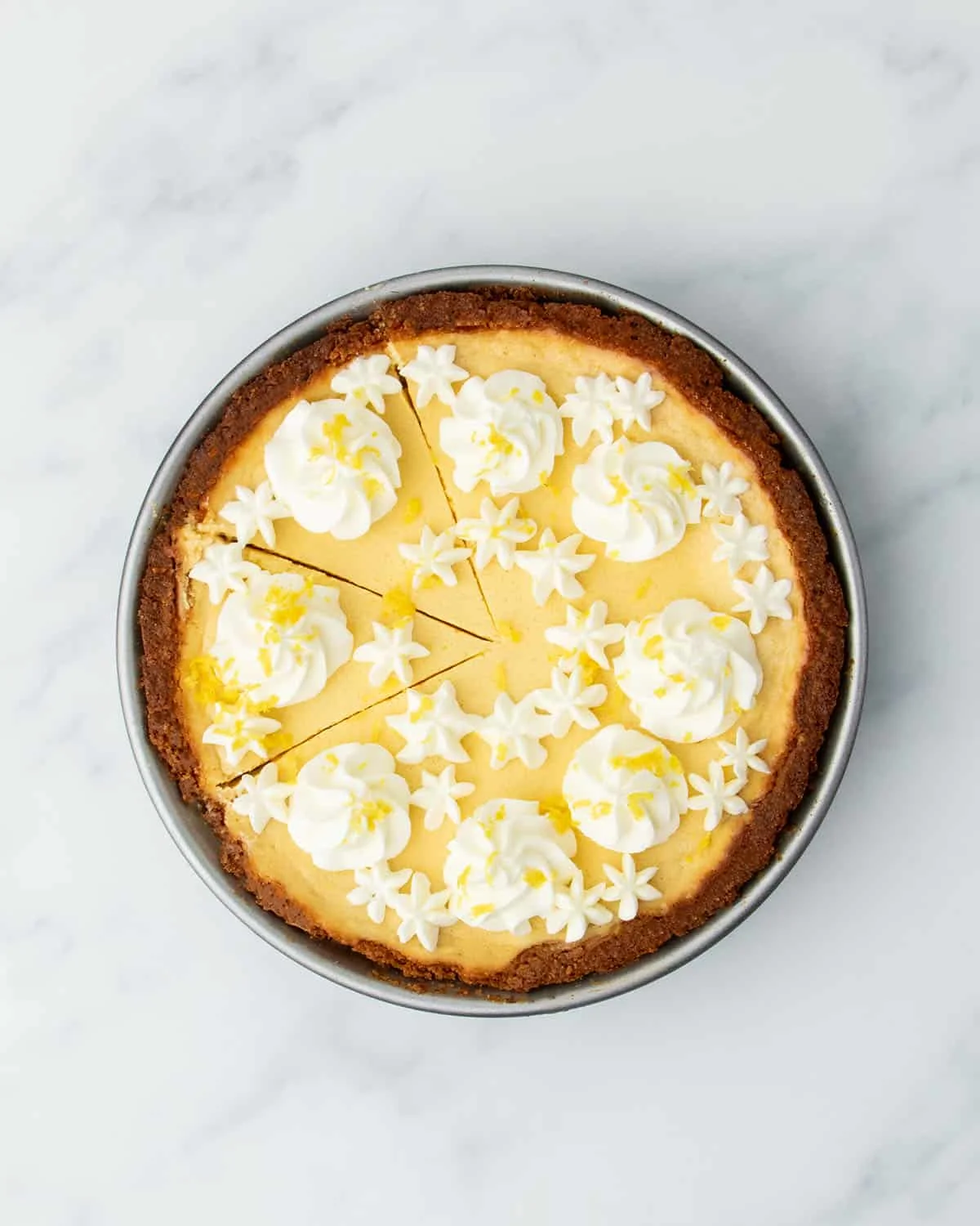 Fully baked lemon pie decorated with piped whipped cream and lemon zest, with a few slices cut but not removed.