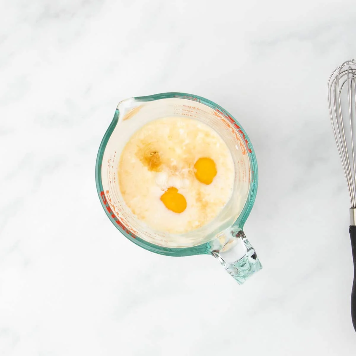 Glass measuring cup filled with dairy free milk, eggs, dairy free yogurt, and flavorings like vanilla extract before mixing.