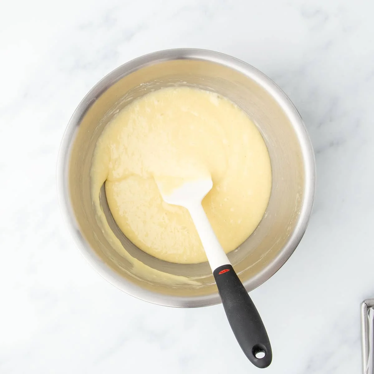 Gluten free cake batter fully mixed and smooth in a large stainless steel mixing bowl with a white silicone spatula.