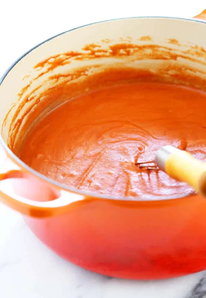 Gluten free enchilada sauce in an orange pot with a whisk in the pot