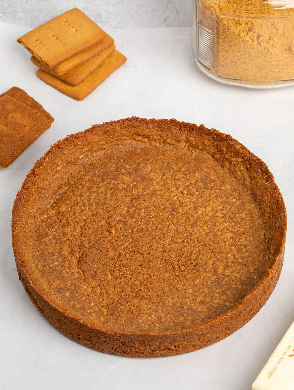 Graham cracker crust on white paper with more graham crackers broken in half and a glass jar with brown crumbs inside.