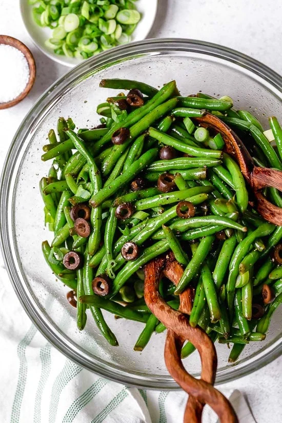 Green beans and olives in bowl with salad tongs.