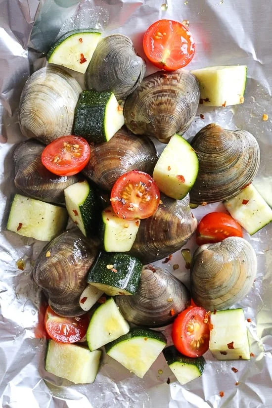Grilled little neck clams cooked in foil packets with zucchini and tomatoes in a garlic white wine sauce, so fast and easy, perfect to make all summer long!