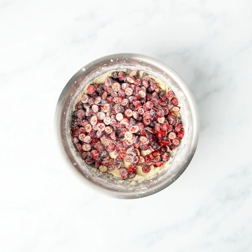 Halved fresh cranberries on top of light yellow batter in bowl