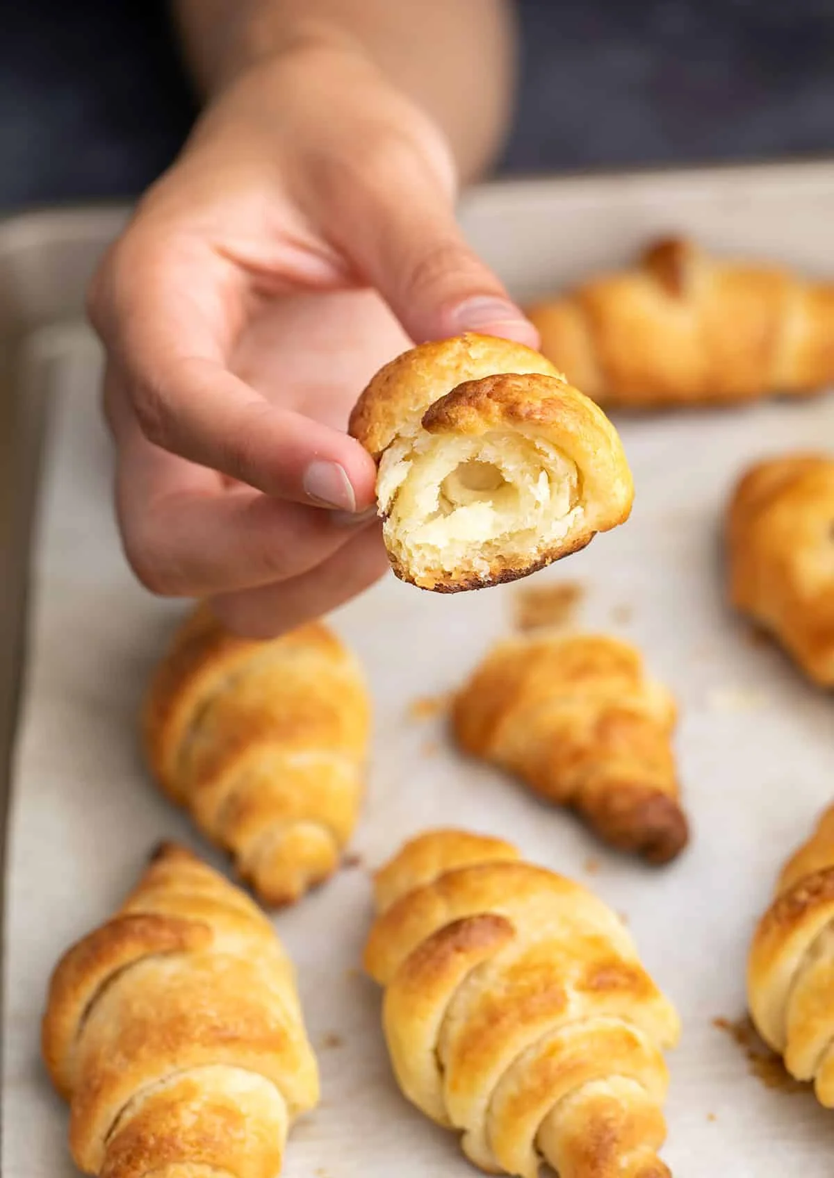 Hand holding broken gluten free croissant over tray of more pastries