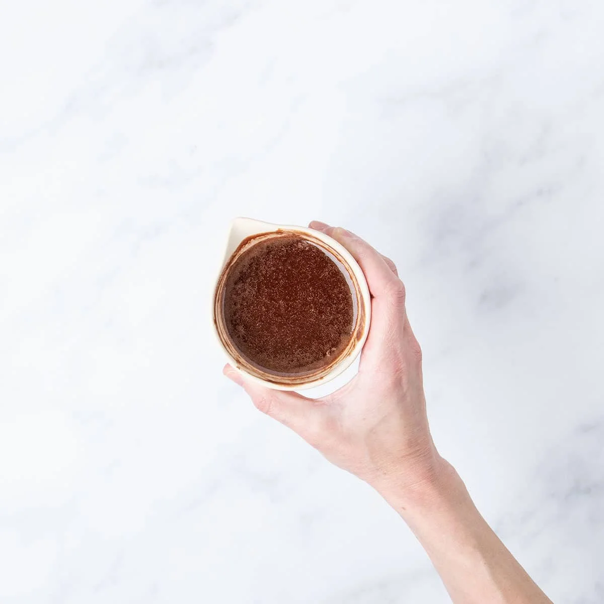 hand holding brown melted chocolate and butter mixture in small light tan ceramic bowl