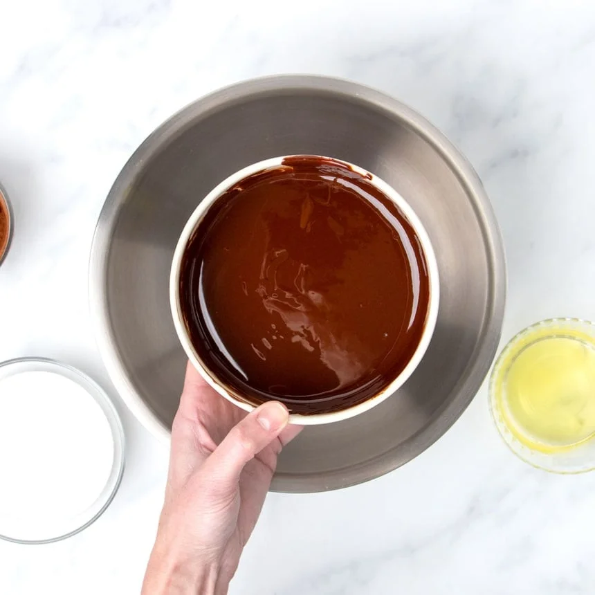 Hand holding melted chocolate and butter in small bowl.