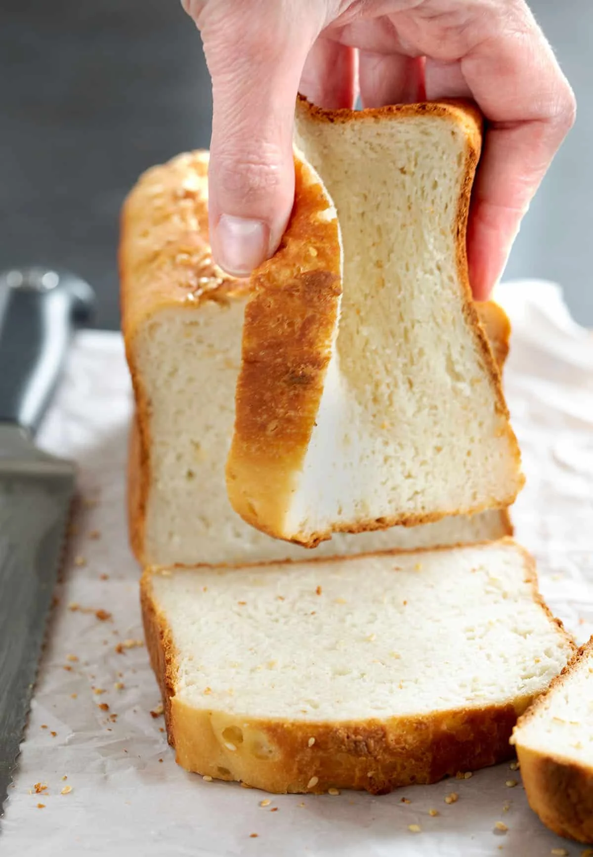 Hand holding slice of brown crust with soft white interior bread squishing it.