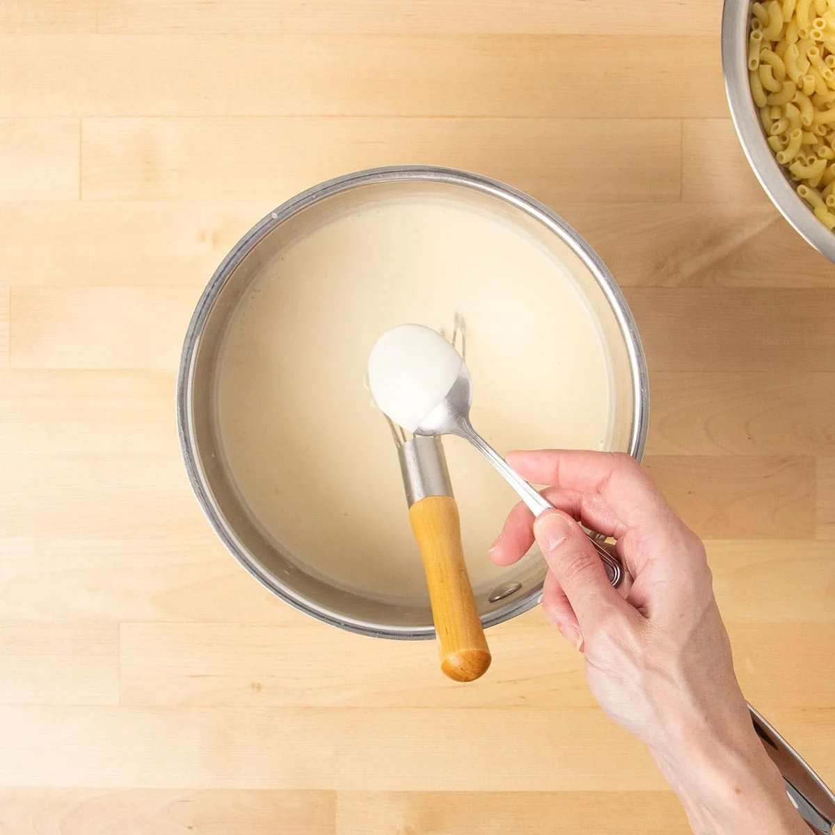 Hand holding spoon with light tan sauce.