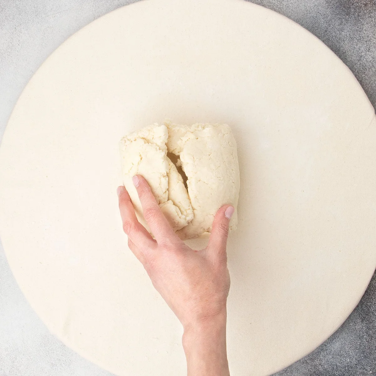 Hand holding together folded dough into square packet on tan cloth.