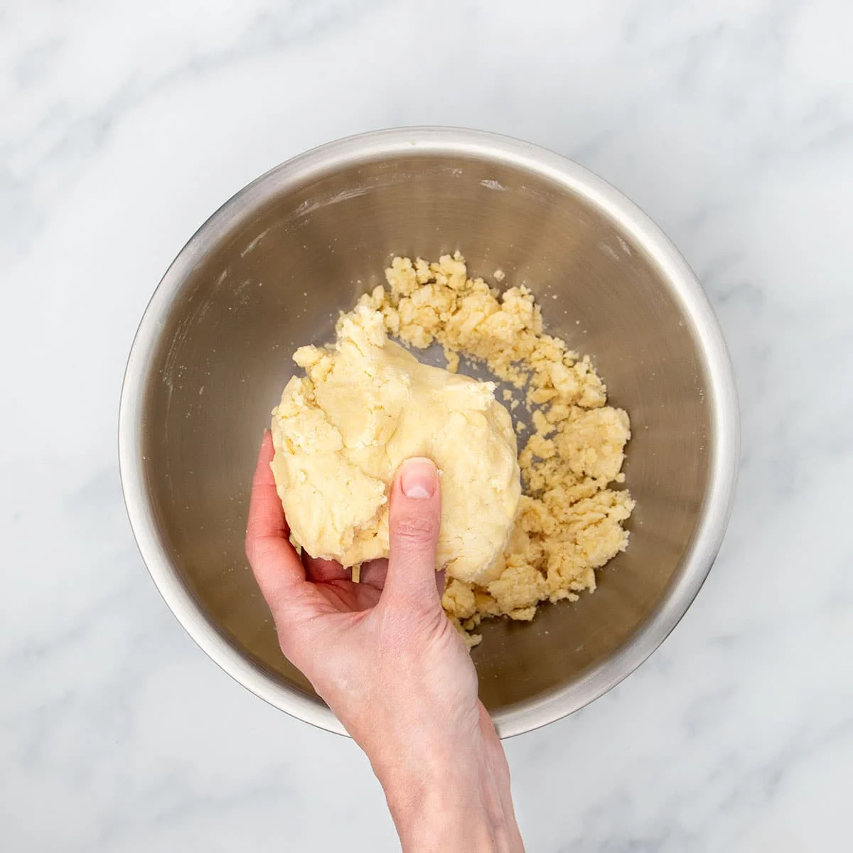 Hand holding very pale yellow raw sugar cookie dough pressed into a large clump.