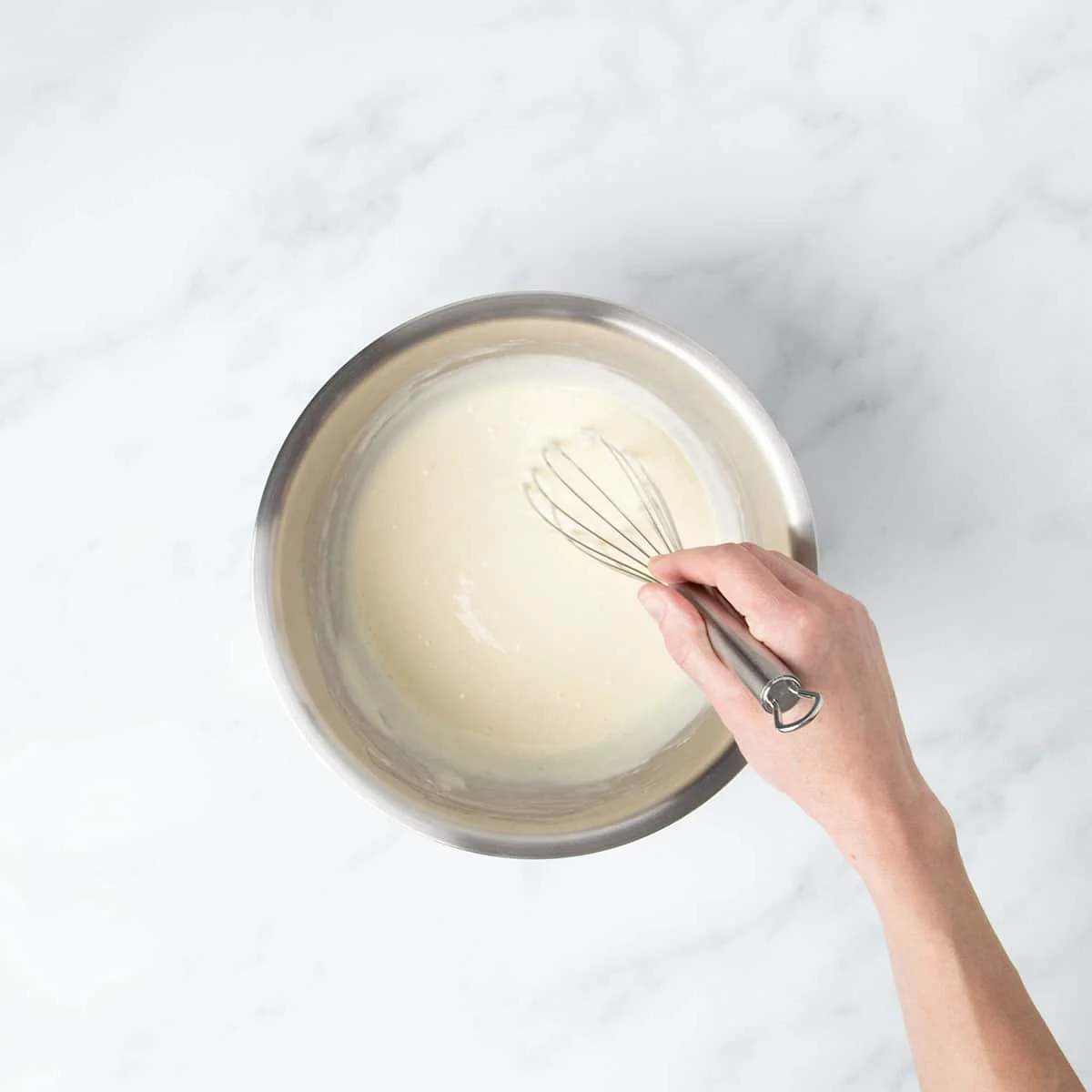 Hand holding wire whisk in pancake batter.