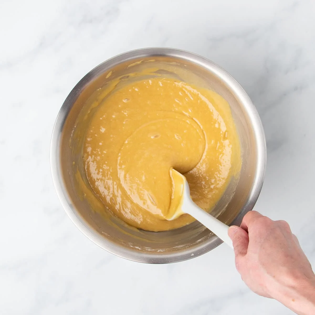 hand mixing light brown gluten free blondie mixture with white silicone spatula in mixing bowl