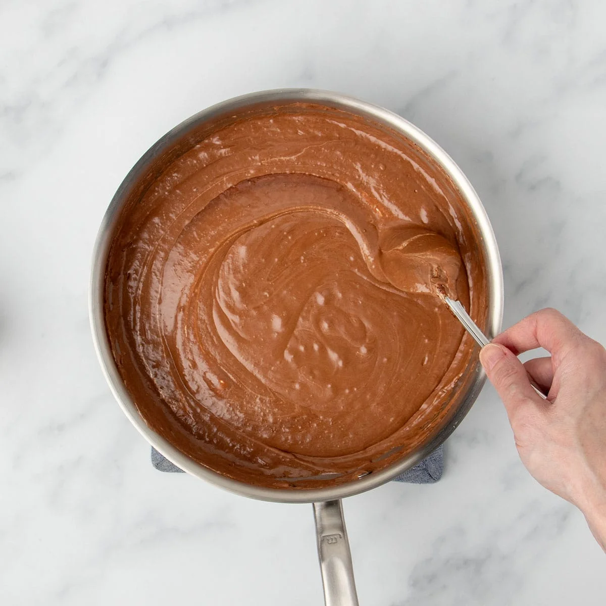 hand mixing light brown thick swirled mixture in pan, mixing in marshmallow cream