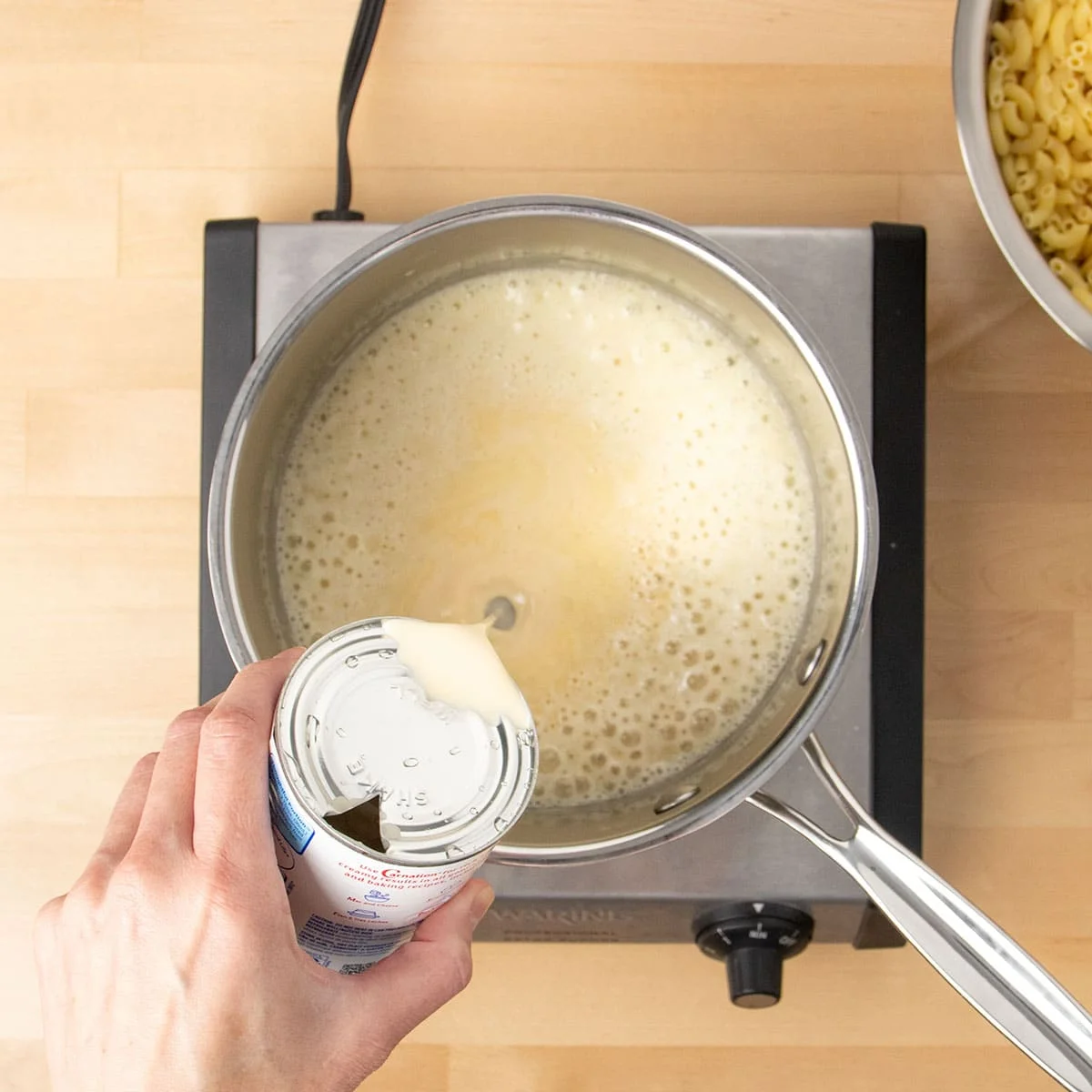Hand pouring evaporated milk into a metal saucepan.