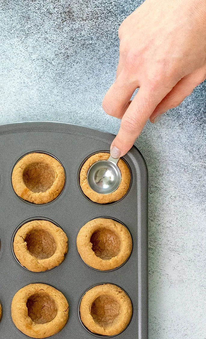 Hand pressing the bowl of a teaspoon into a cookie in a mini muffin tin