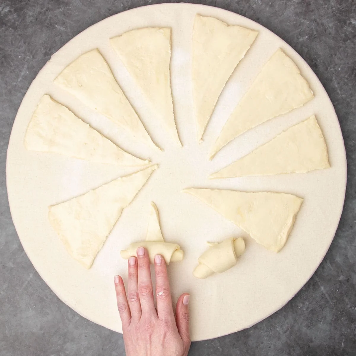 hand rolling one triangle of dough from base to tip with other triangles separated on cloth covered board