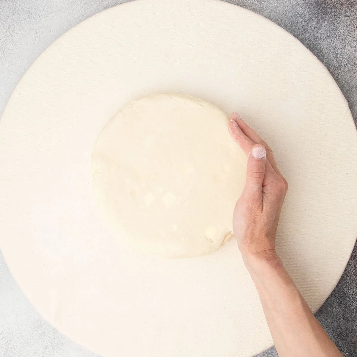 Hand shaping tan raw scone dough into a round on tan cloth.