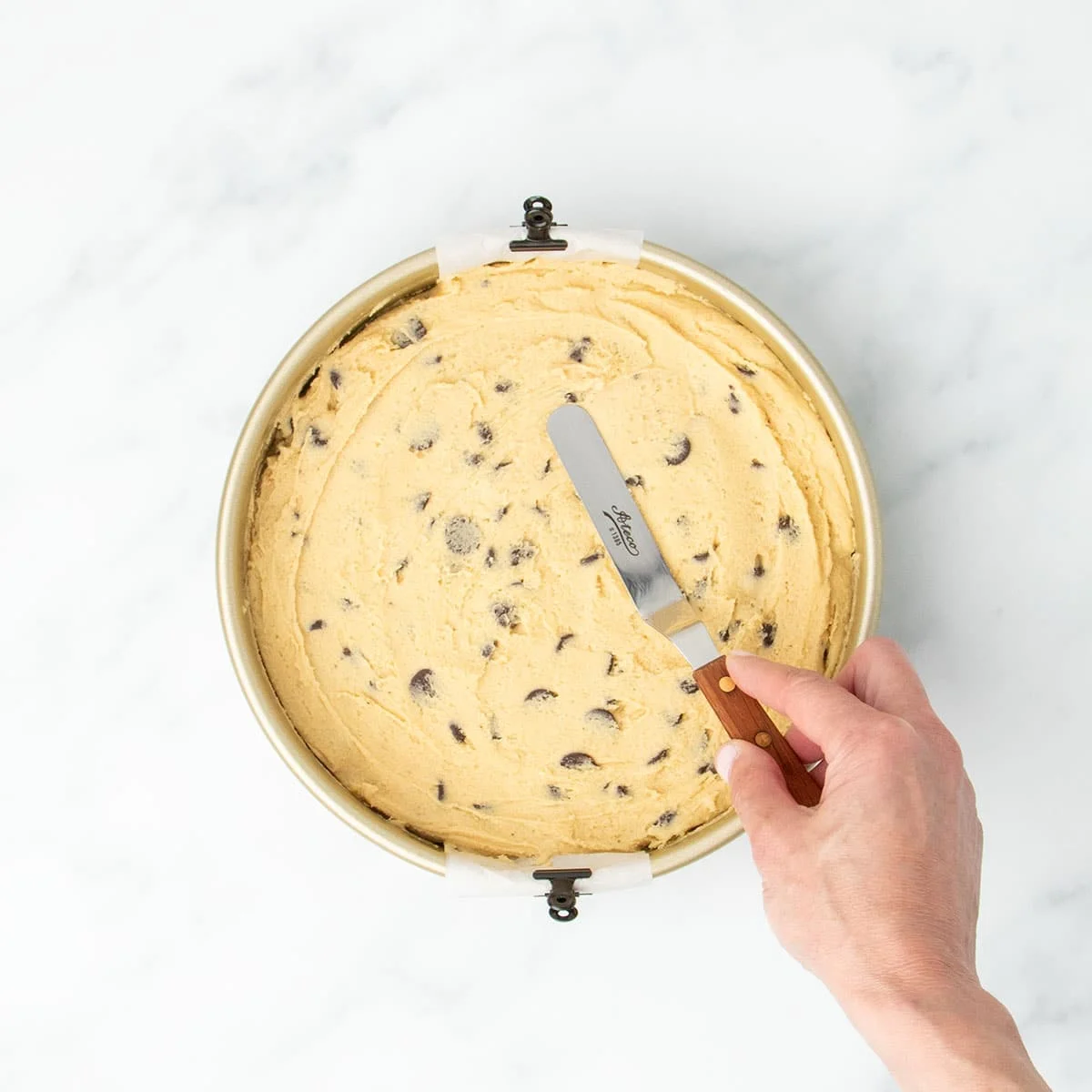 Hand smoothing dough evenly in the pan using an offset spatula with a brown handle
