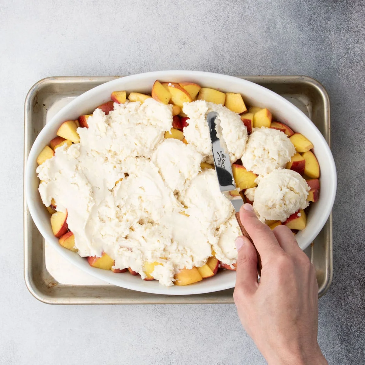 Hand using an offset spatula to spread dough evenly over the peach filling.